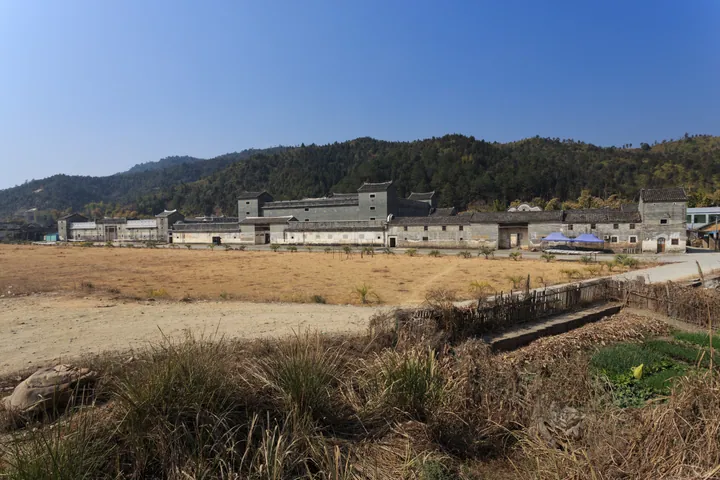 A long grey walled compound with tower-like corners set against forested hills