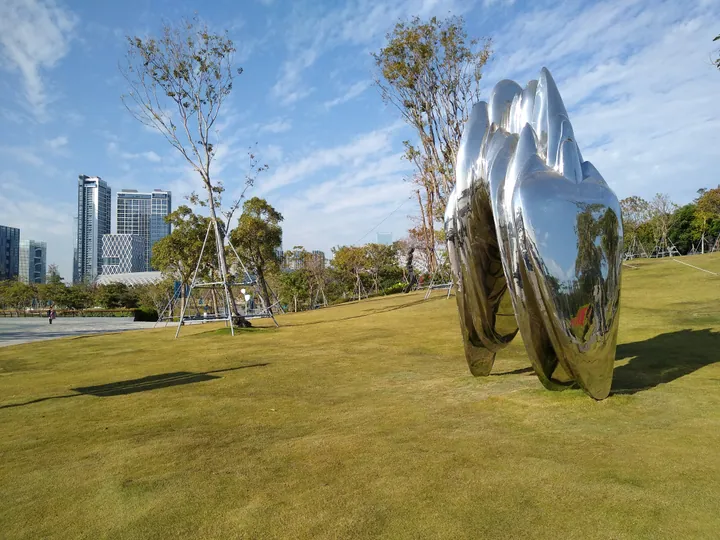 Reflective abstract sculpture on open grass with the Shenzhen skyline behind