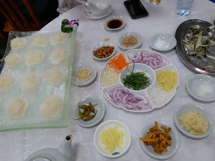 Thin raw fish slices on a glass tray next to many small dishes of garnishes