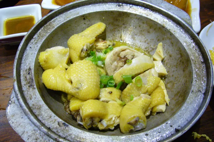 Pieces of Dongjiang-style salt-baked chicken in a metal pot with scallions