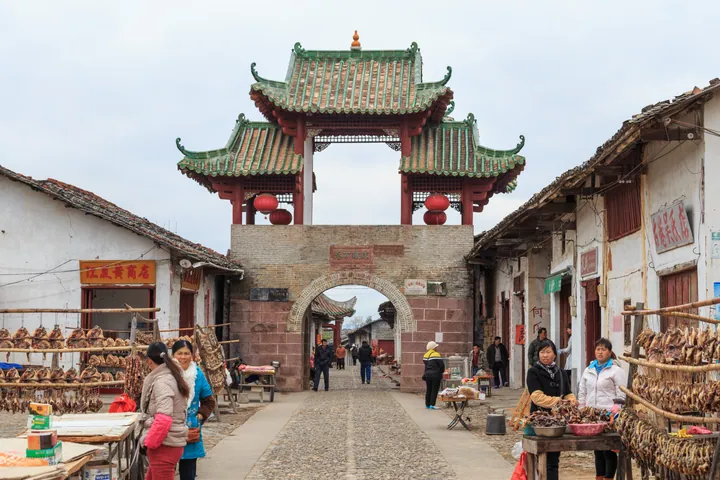 A red and green pagoda-style gate tower spanning the old street of Zhuji Lane, with market stalls on either side