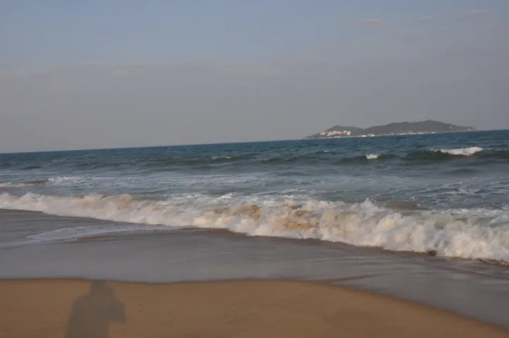 Waves rolling onto the sand at Haitang Bay with a hazy island in the distance