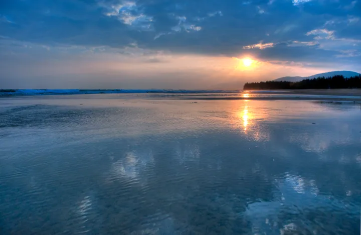 The sun setting over a calm bay, reflected on wet sand