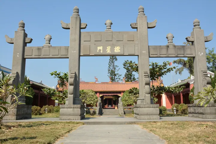 Ornate stone archway framing a red-roofed temple hall under a clear blue sky