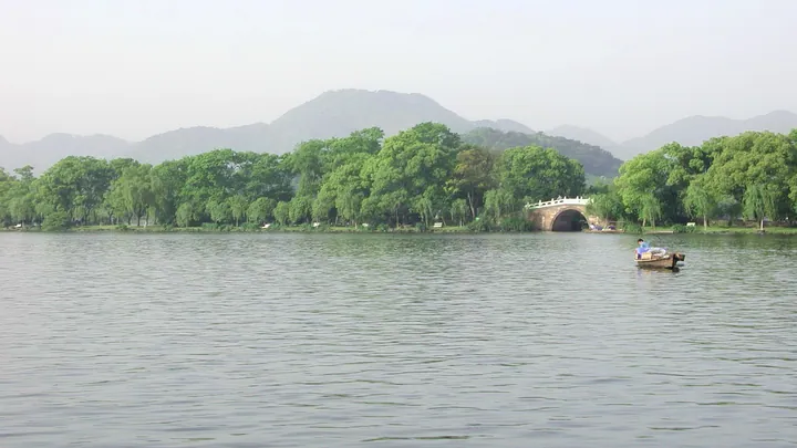 Lake, trees, and a stone arch bridge with hills in the background at West Lake