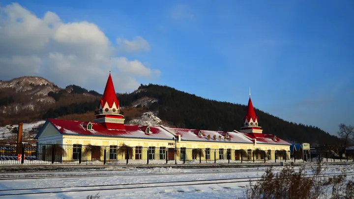 Red-roofed railway station building with twin spires under a blue sky and snow