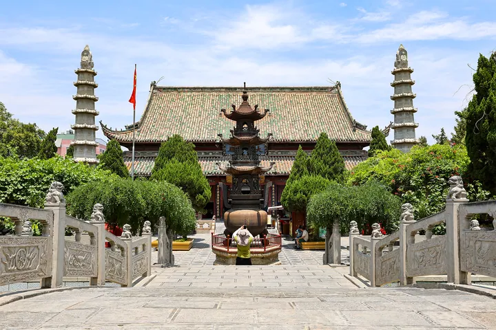 Ornate multi-tiered temple hall flanked by two stone pagoda towers under a blue sky
