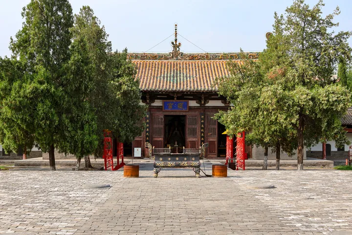 Temple hall with a green-glazed roof framed by tall trees