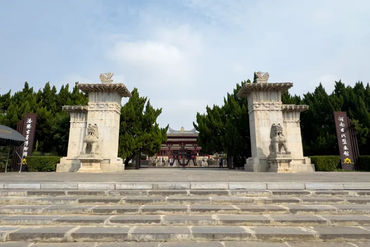 Stone entrance gateway with carved lion statues leading to a red-roofed museum building.