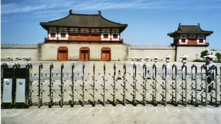 Reconstructed red and grey city gate tower behind a crowd-control fence
