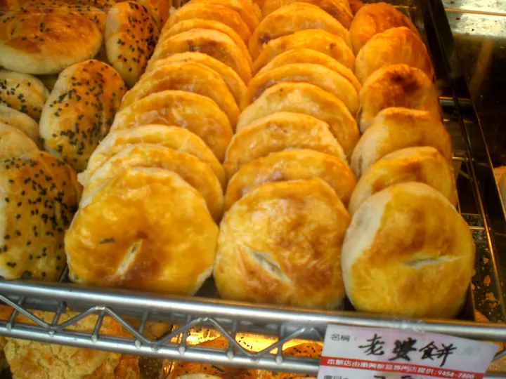 Rows of round golden wife cakes in a bakery display case.