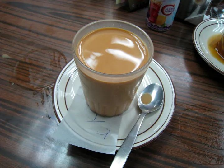 A glass of Hong Kong-style milk tea on a saucer with a spoon.