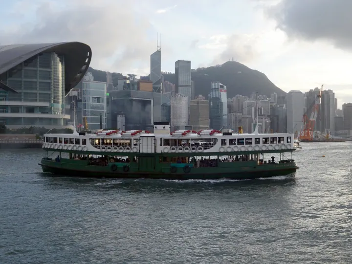 Green and white double-deck ferry boat on the harbour with skyscrapers behind