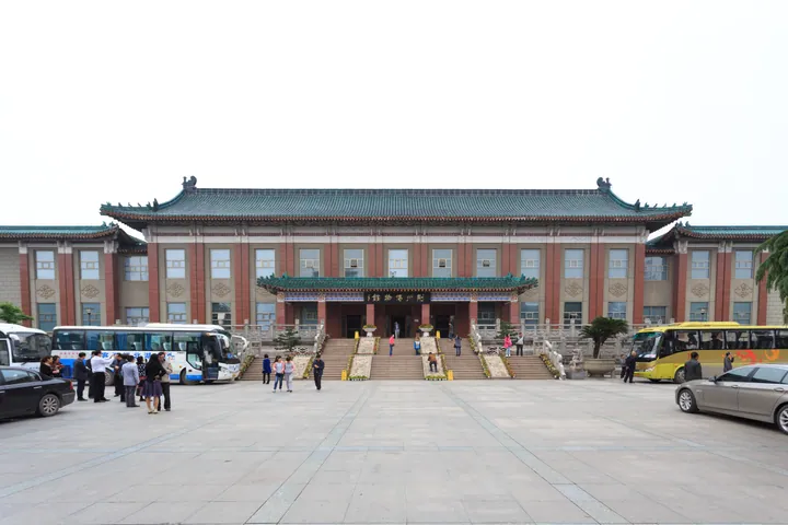 The green-roofed entrance building of Jingzhou Museum with tour buses parked outside