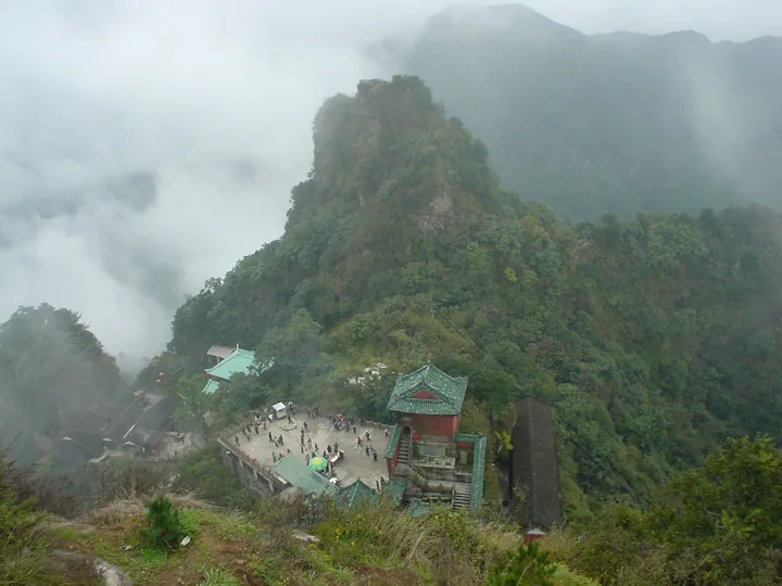 Small red-roofed temple perched on a rocky, mist-shrouded mountain peak