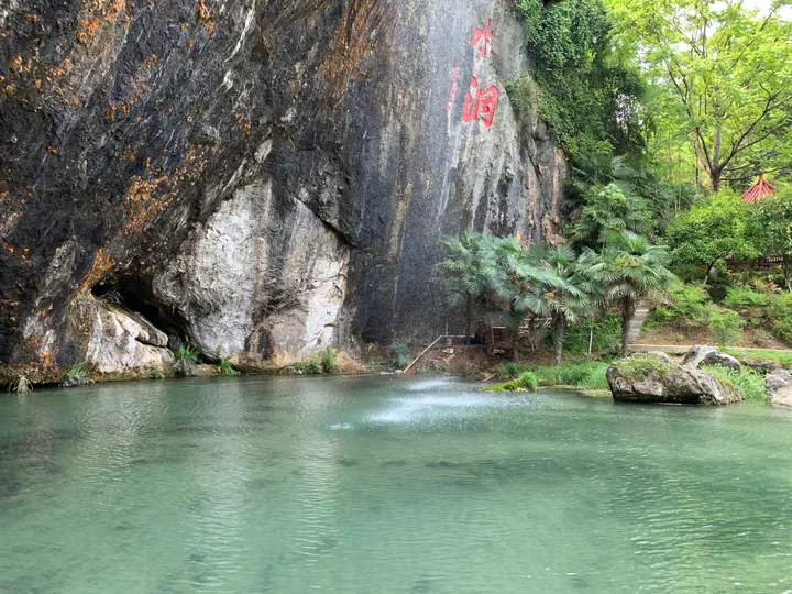 A cliff with carved characters above a turquoise pool at a cave entrance