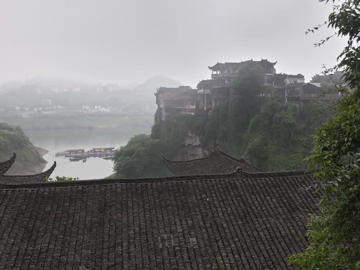 Misty view of Furong Town's cliffside stilted buildings above the river
