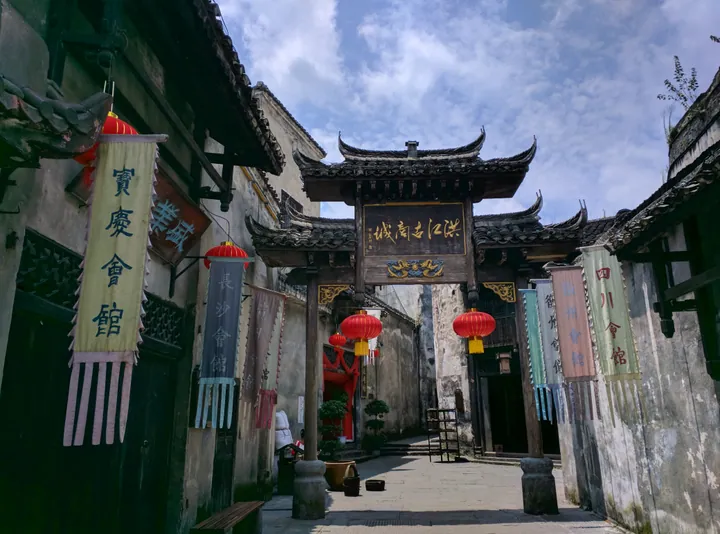 Ornate wooden gate archway decorated with red lanterns and hanging guild-hall banners