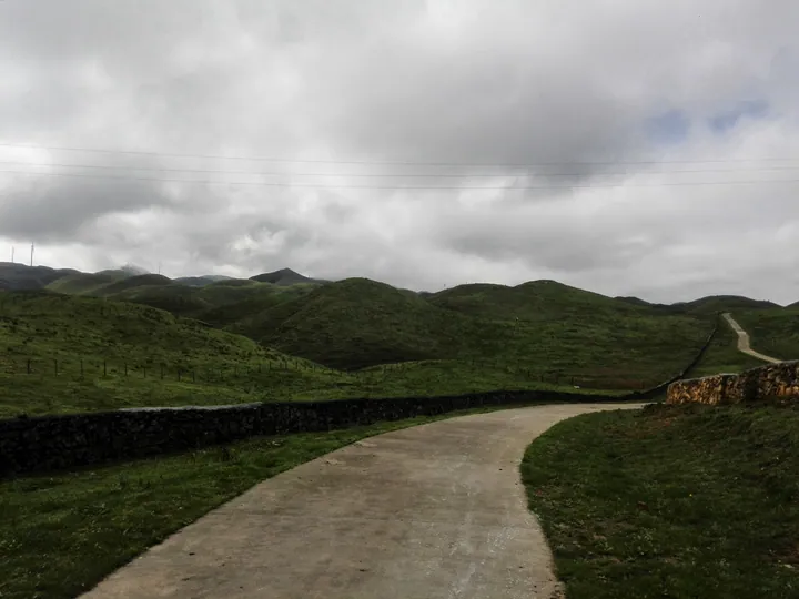 A paved road curving through green rolling hills under a cloudy sky