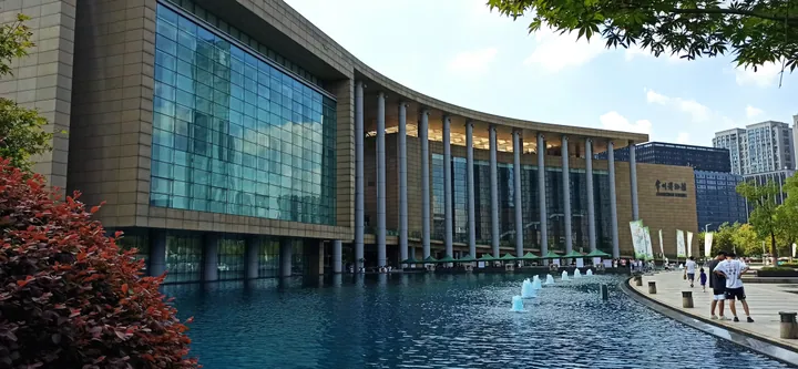 Curved museum building with a columned facade beside a fountain pool under a blue sky