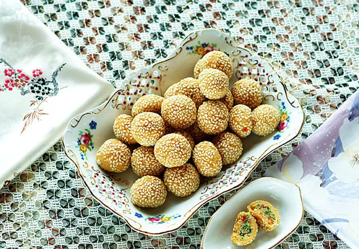 Bowl of sesame-coated pastry balls with one cut open showing the filling