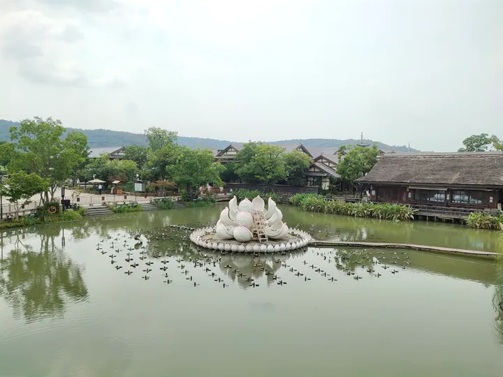 Lotus-shaped sculpture floating on a lake surrounded by traditional wooden buildings