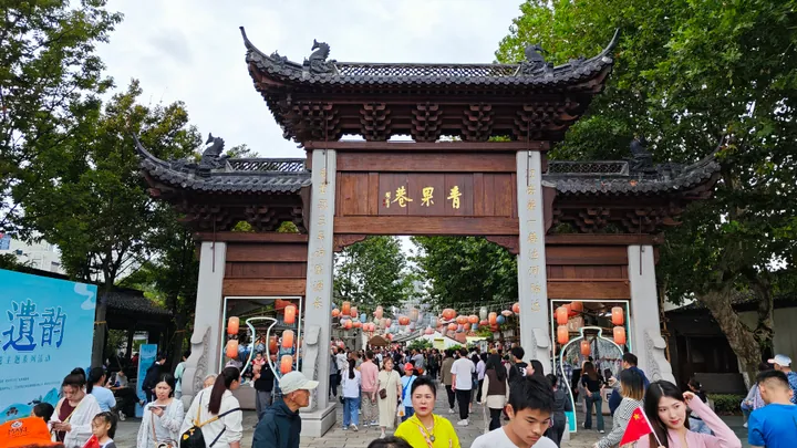 Wooden gate arch marked Qingguo Lane with visitors walking underneath.