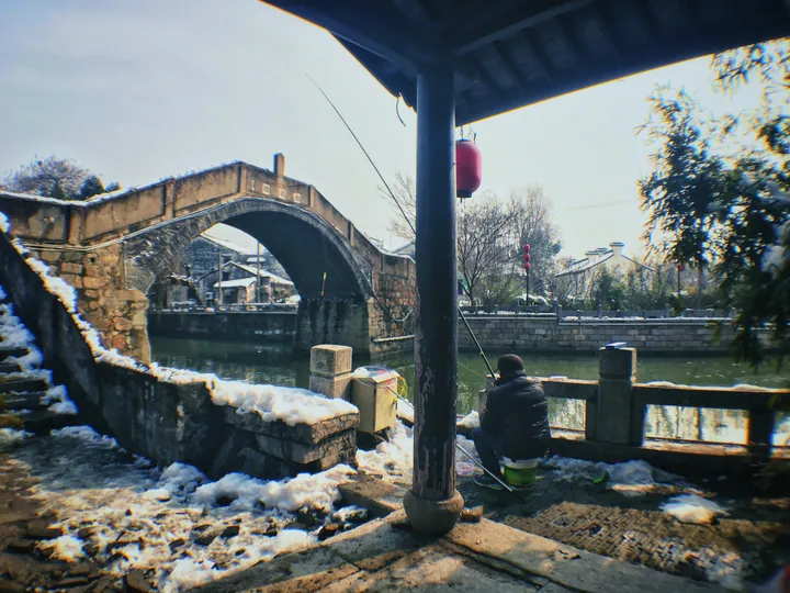 Old stone arch bridge over a canal with snow on the ground