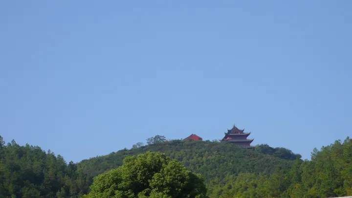 Red temple building on a tree-covered mountain peak against a blue sky