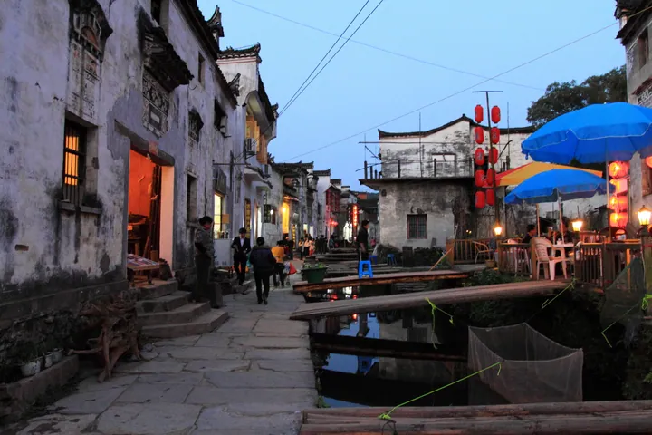 A dusk street scene along a stone canal lined with old houses and lanterns