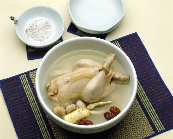 A whole chicken in ginseng soup with jujubes in a white bowl