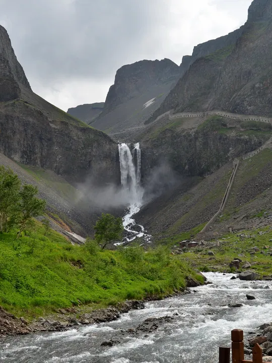 A tall twin waterfall dropping between steep mountain cliffs into a rushing stream