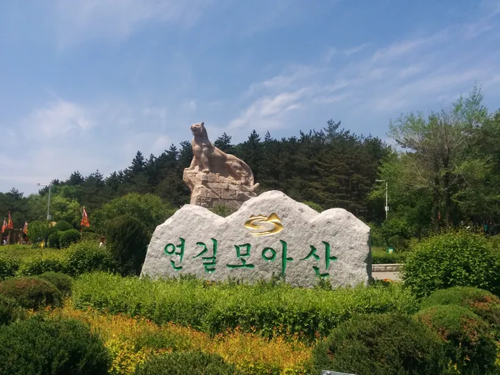 Carved stone marker reading '延吉帽儿山' topped by a tiger statue amid greenery