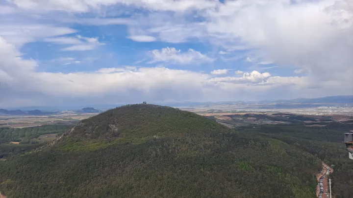 Forested rounded mountain peak seen from an elevated viewpoint under a partly cloudy sky
