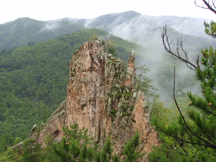 Jagged granite spire rising above misty forested mountains at Xianjingtai