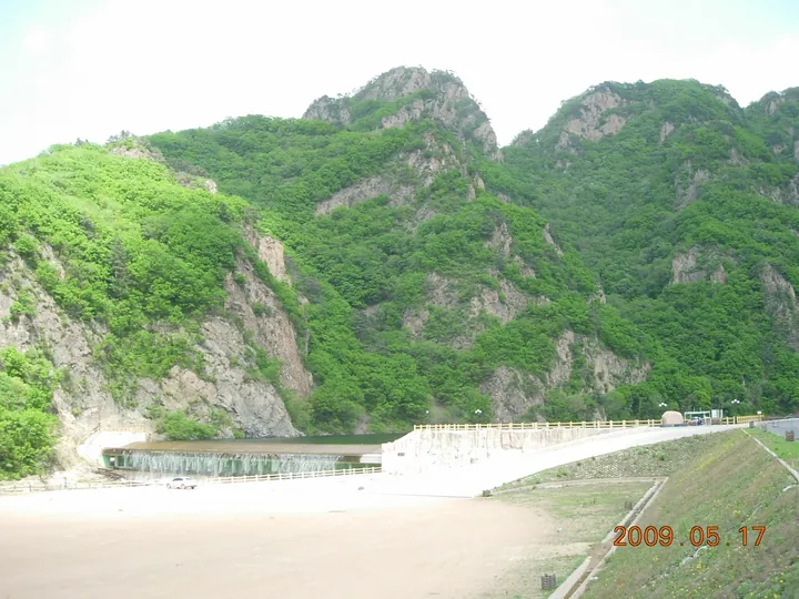 Green forested mountain peaks rising above a reservoir and dam near the entrance of Guanmenshan