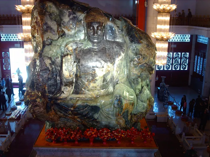 Large natural jade boulder carved into a seated Buddha figure, displayed indoors