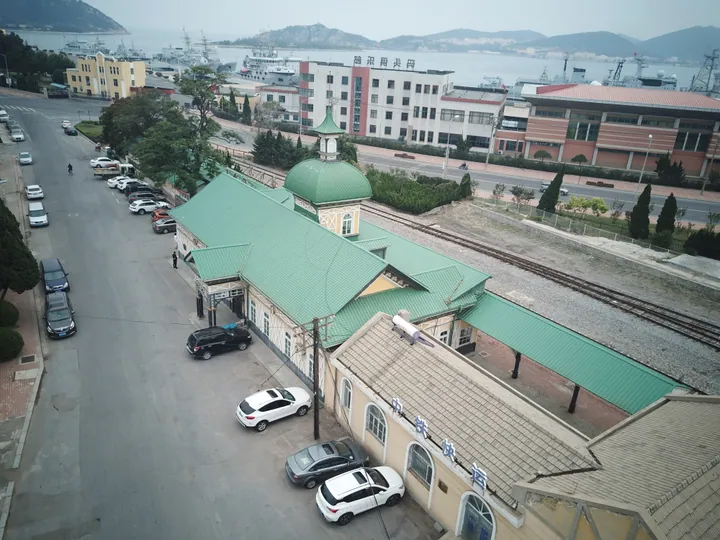 Aerial view of the green-roofed Lüshun Railway Station building with harbor and hills beyond
