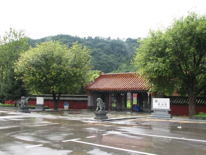 Red gatehouse with stone lion statues and a bilingual sign reading Qing Yongling Tomb