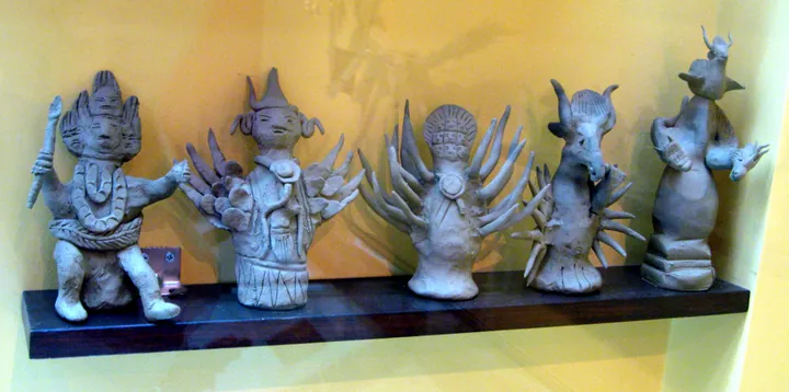 A row of small clay figurines representing Naxi deities on a museum shelf