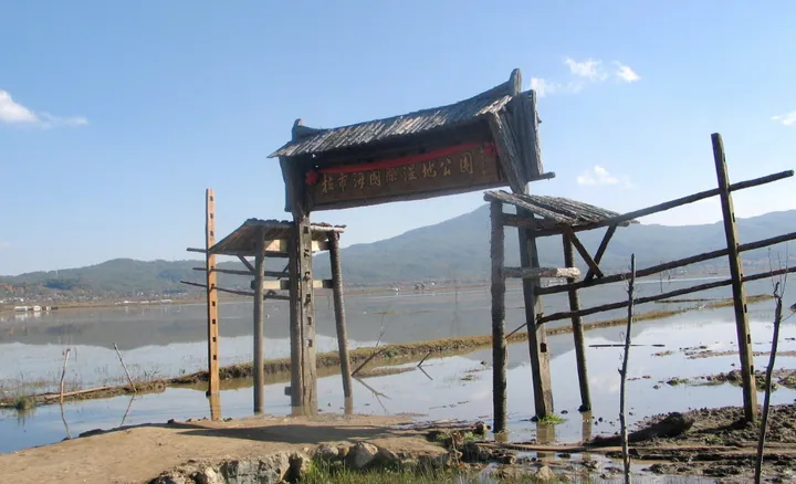 Rustic wooden gate structure with a sign reading Lashihai Wetland Park beside a wetland