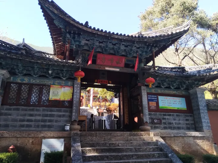 Ornate temple gate with upturned eaves, a name plaque, and red lanterns