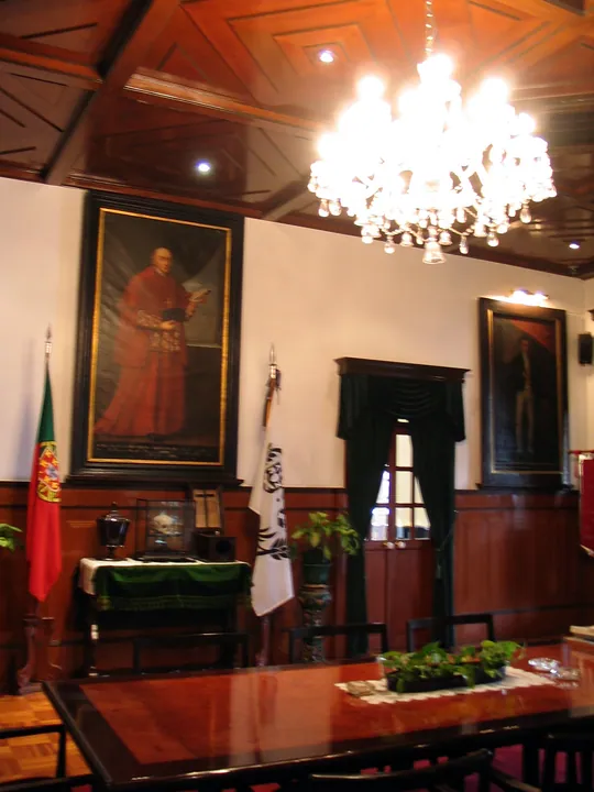 Interior room of the Museum of the Holy House of Mercy in Macau, showing portrait paintings on the walls, a chandelier and a glass display case