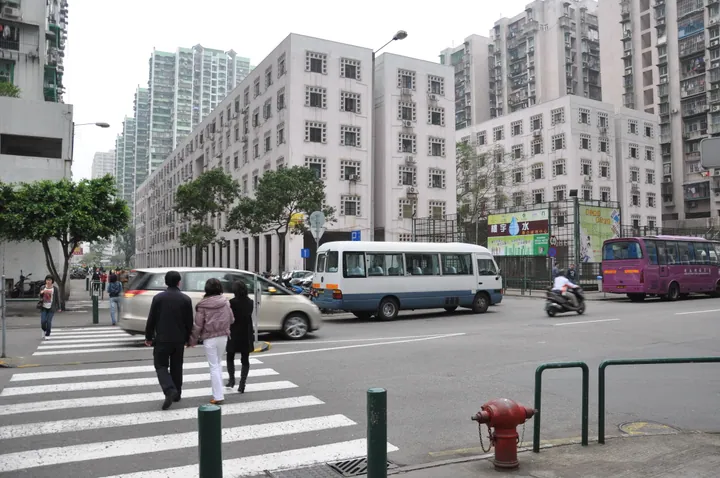 A city street with pedestrians and a minibus, flanked by mid-rise public housing blocks.