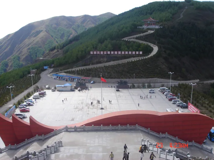 Museum plaza with a curved red roof structure, flagpole, and hillside pavilion behind