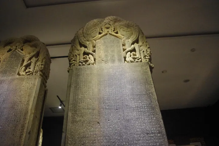 Tall carved stone stele with a dragon-decorated top, displayed inside a museum gallery