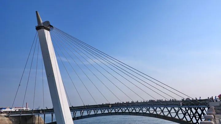 White sail-shaped cable-stayed bridge over water under a clear blue sky.