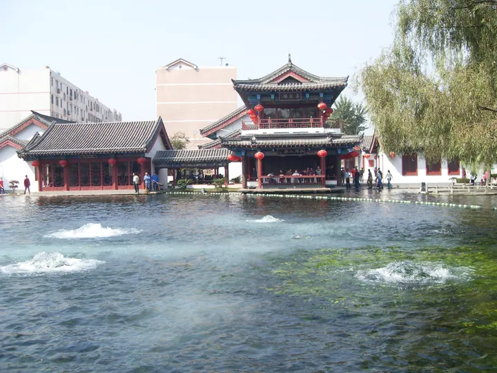 Traditional lakeside pavilions beside bubbling spring water in a park