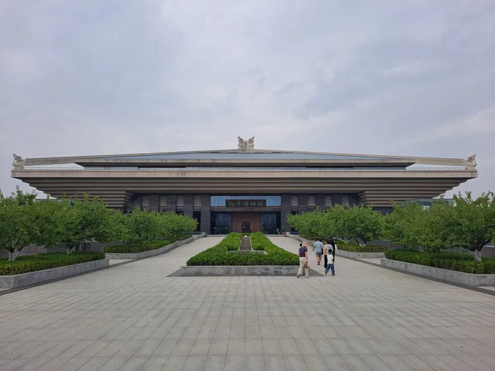 A long low modern museum building with a sweeping roofline behind a landscaped plaza