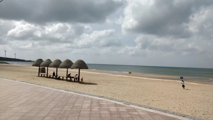 Row of thatched-roof beach shelters on the sand at Naxianghai, with the sea behind